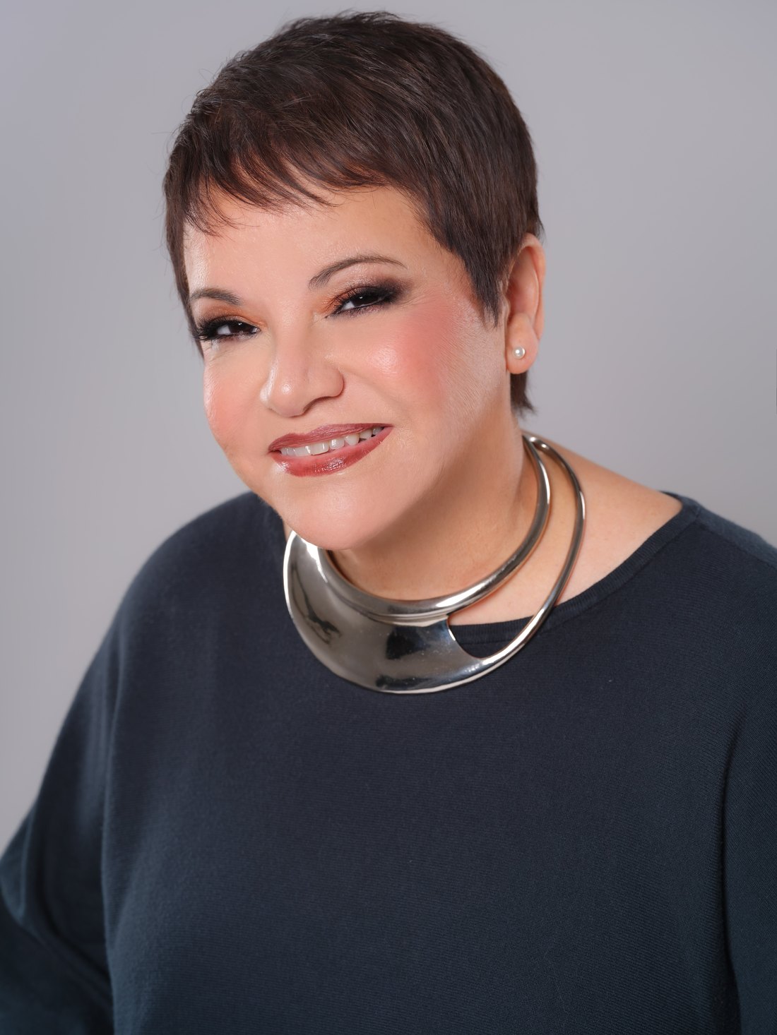 Dr. Lourdes Ramos Rivas smiling, wearing a navy sweater and a silver collar necklace